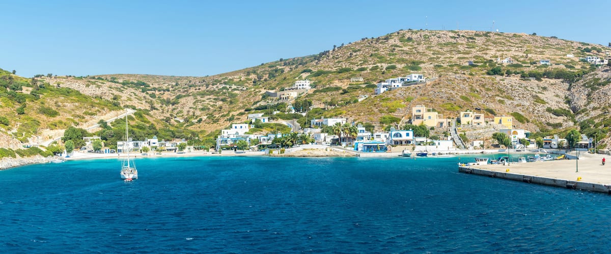 A coastal town with buildings on a hillside, a clear blue sea, and a boat anchored near the shore.