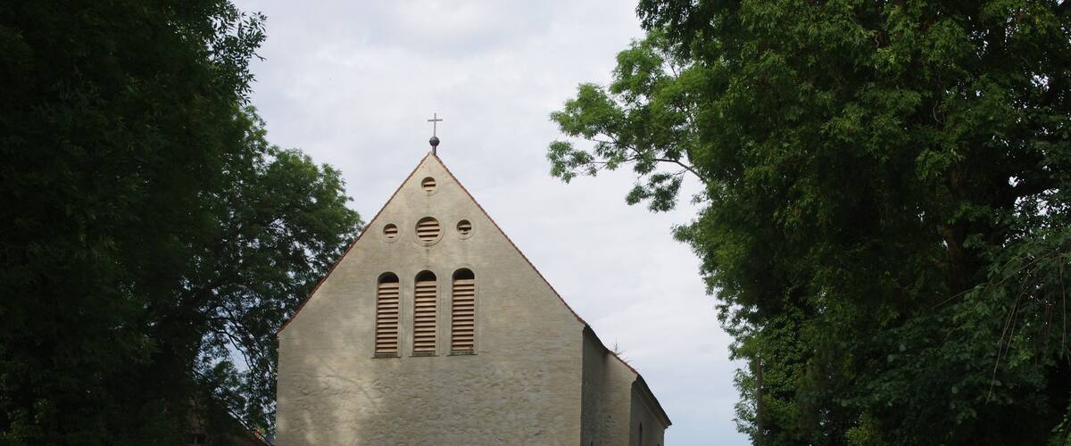 A church with a cross on top, surrounded by trees and a fence.