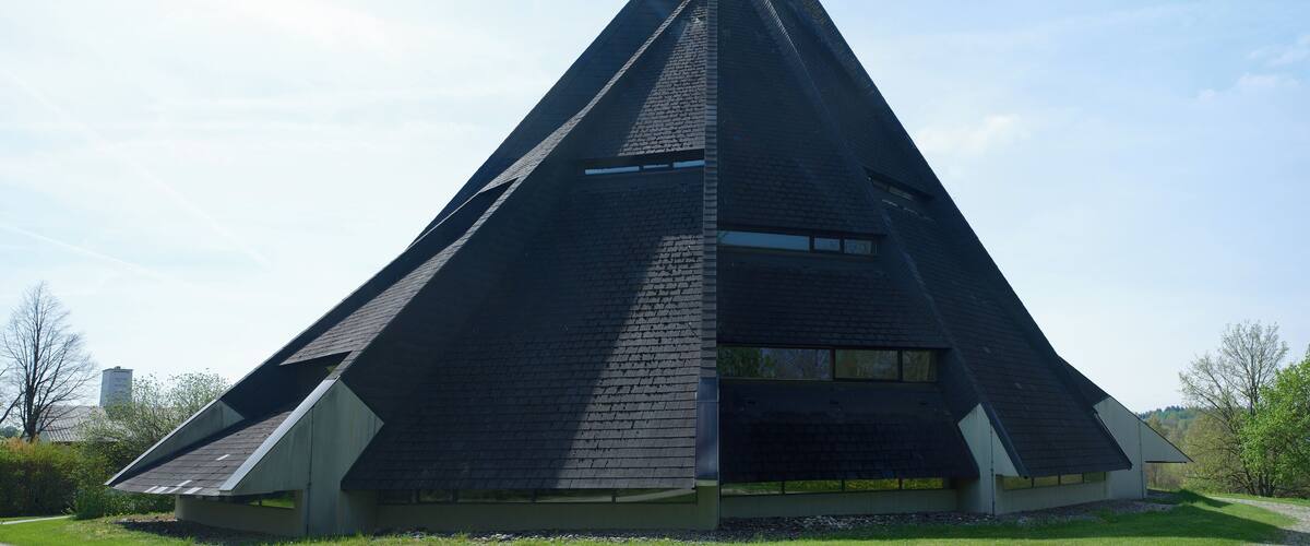 A pyramid-shaped building with a cross at the top, surrounded by grass and trees.