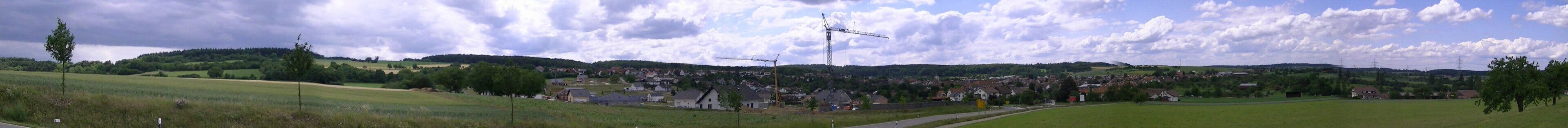 A rural landscape with a wind turbine, houses, and rolling hills.