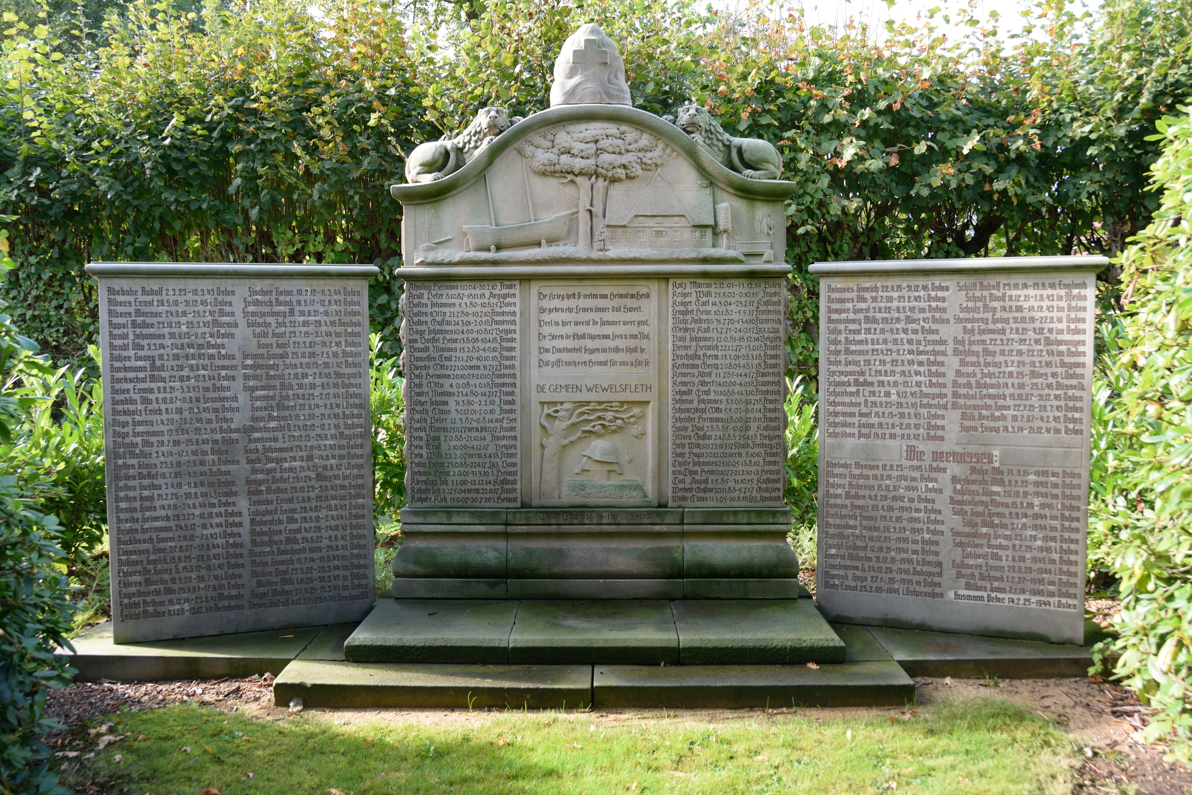A stone monument with inscriptions, surrounded by greenery.