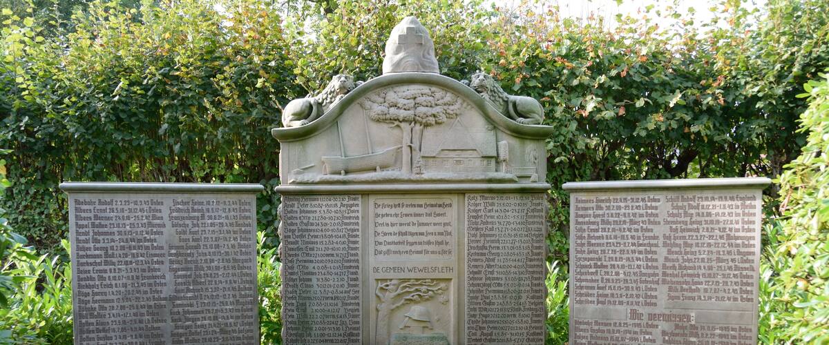A stone monument with inscriptions, surrounded by greenery.