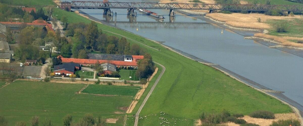 A river with a bridge, green fields, and a small house with a red roof.
