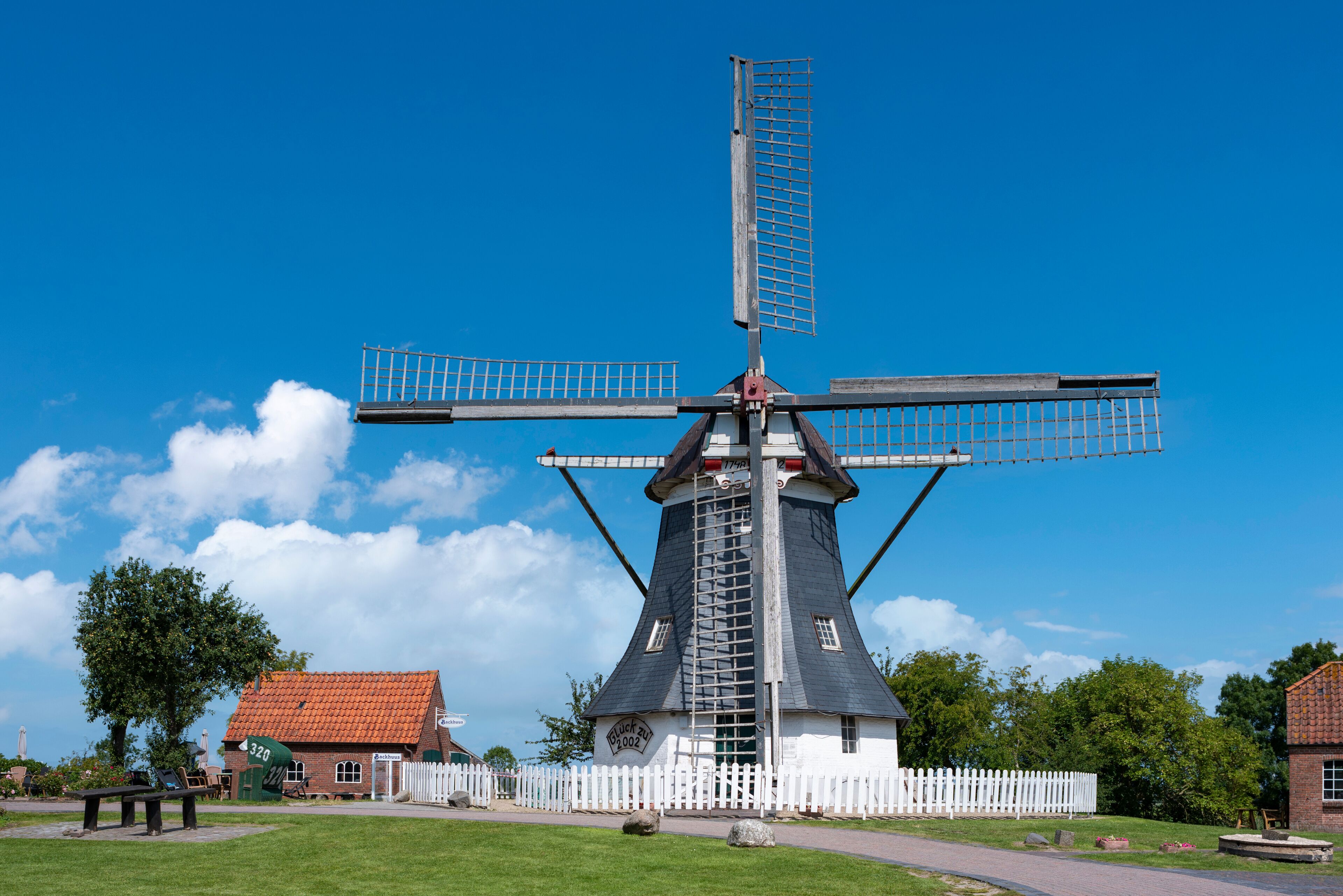 A traditional windmill with a white fence in the foreground and a clear blue sky.