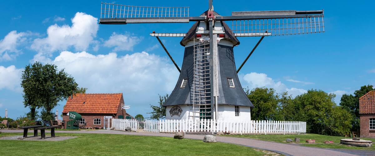 A traditional windmill with a white fence in the foreground and a clear blue sky.
