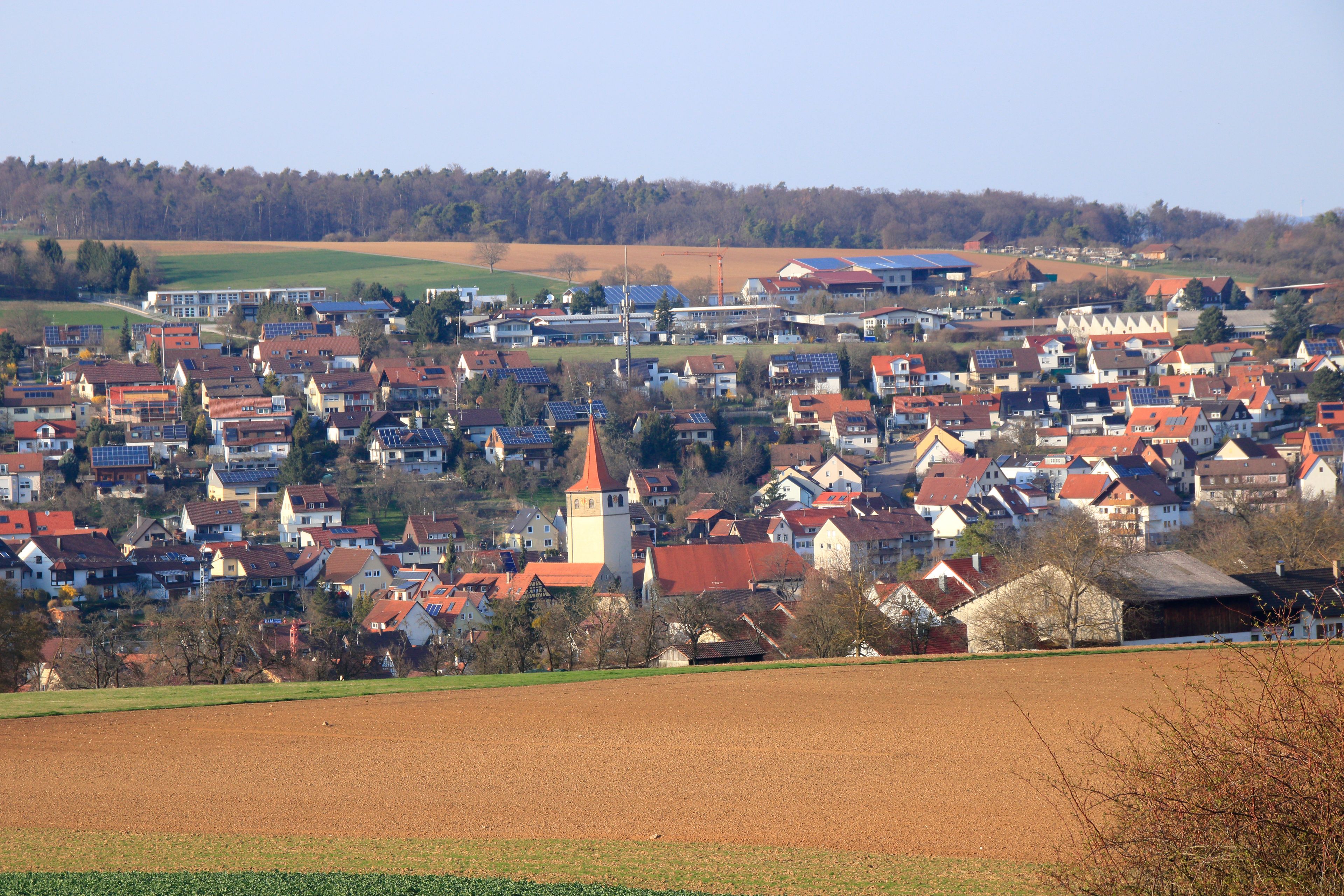 A rural town with red-roofed houses, a church tower, and fields.