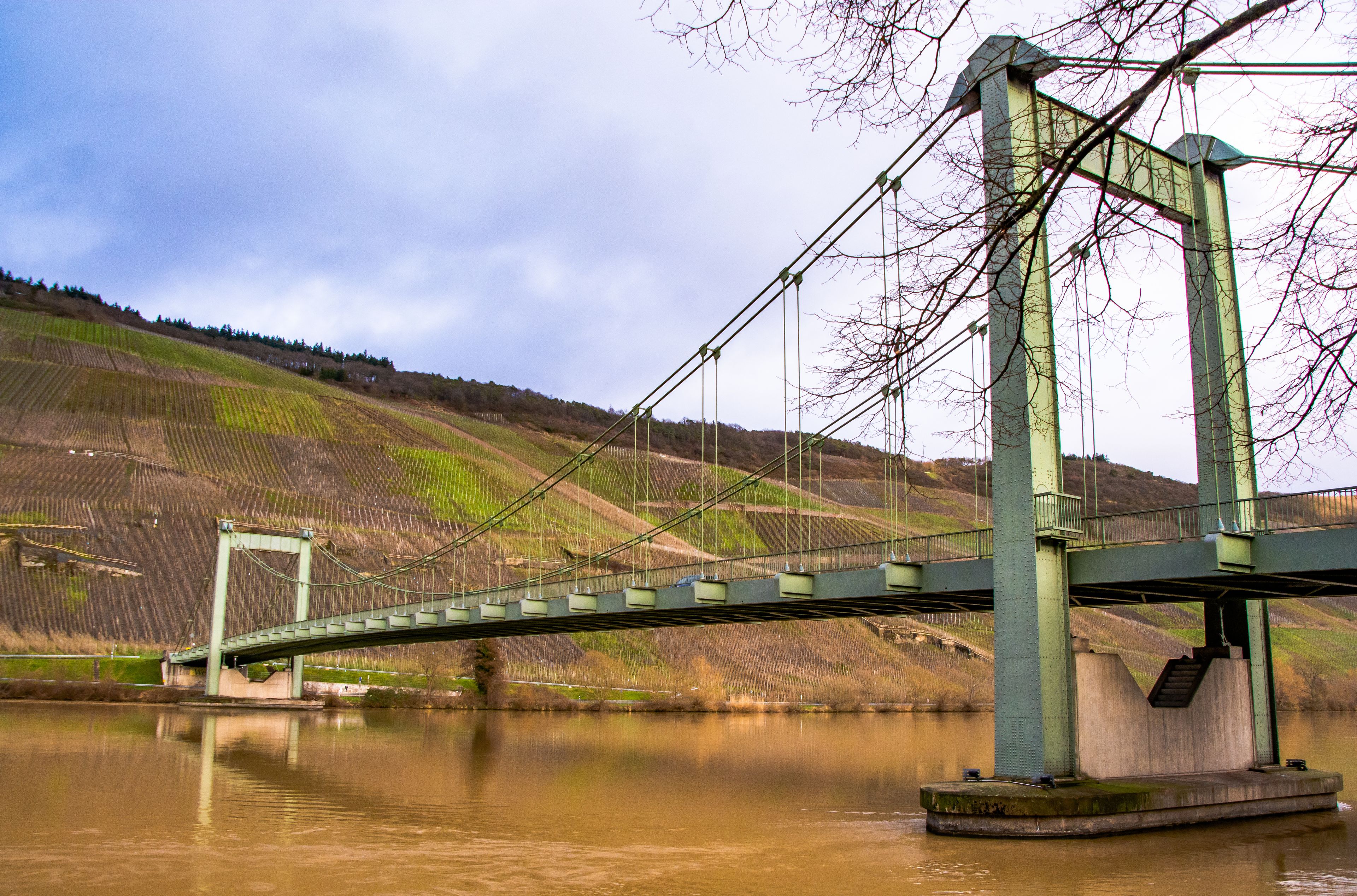 Uma ponte suspensa sobre um rio, com uma paisagem montanhosa ao fundo.