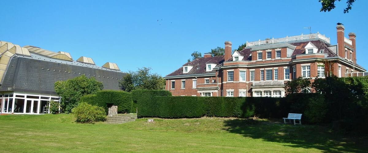 A large brick building with a green lawn and a bench.