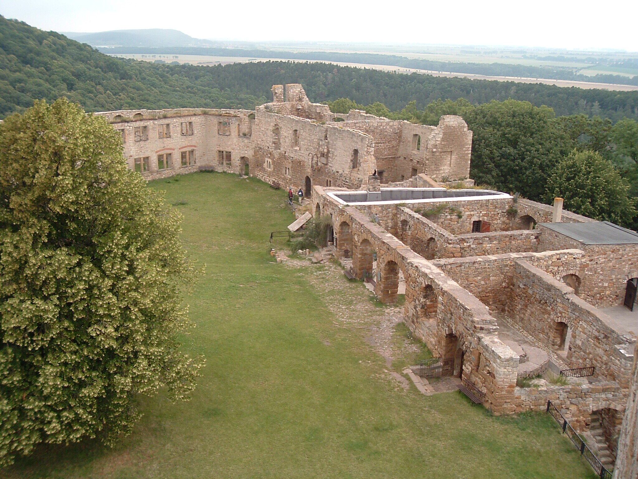 An ancient stone castle with a grassy courtyard surrounded by trees.