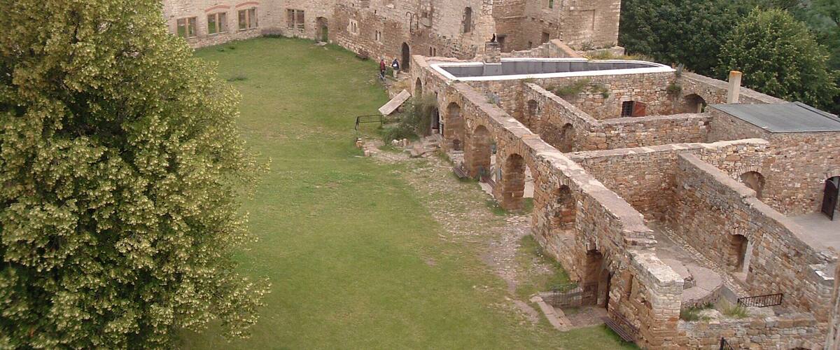 An ancient stone castle with a grassy courtyard surrounded by trees.
