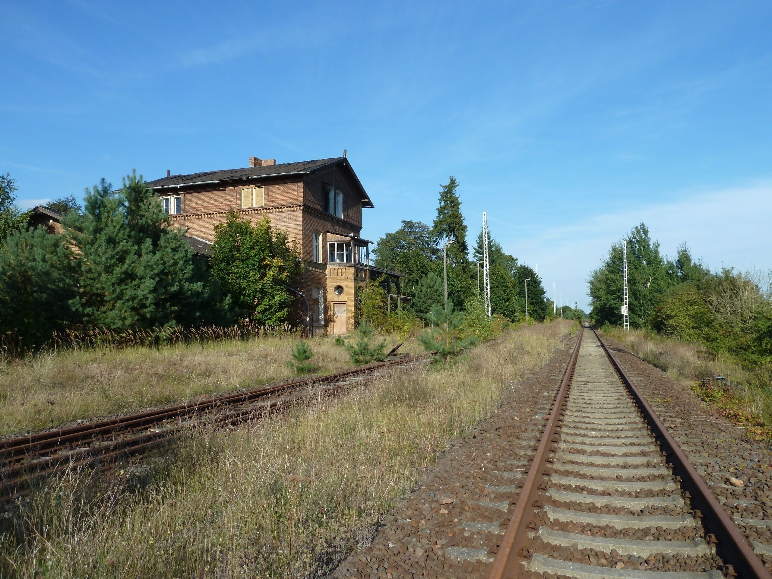 A railway track with a brick building and trees in the background.