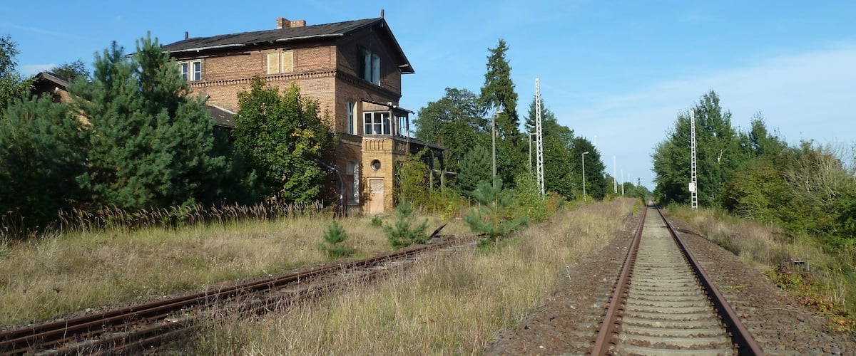 A railway track with a brick building and trees in the background.