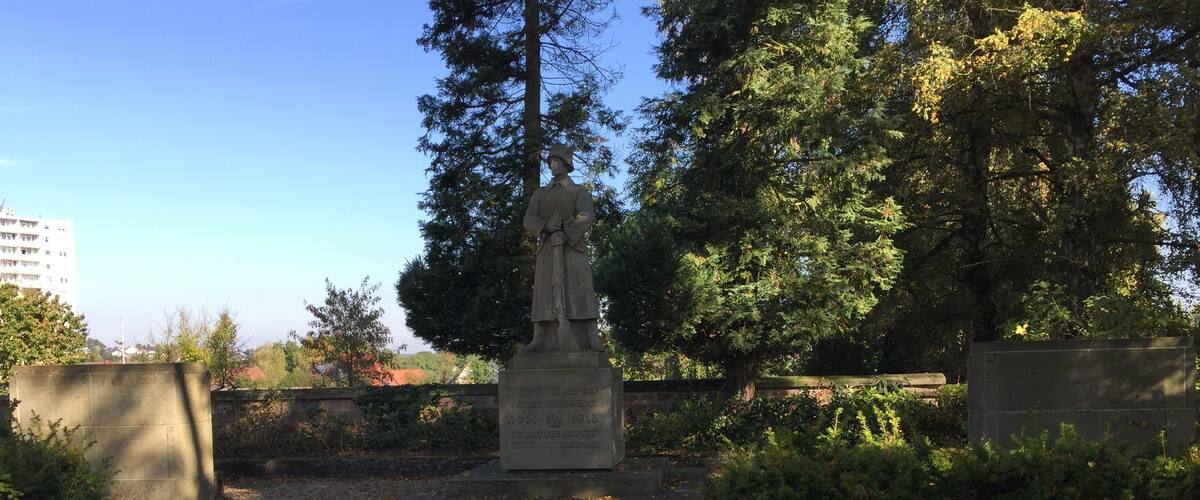 A statue in a park with trees and a stone wall.