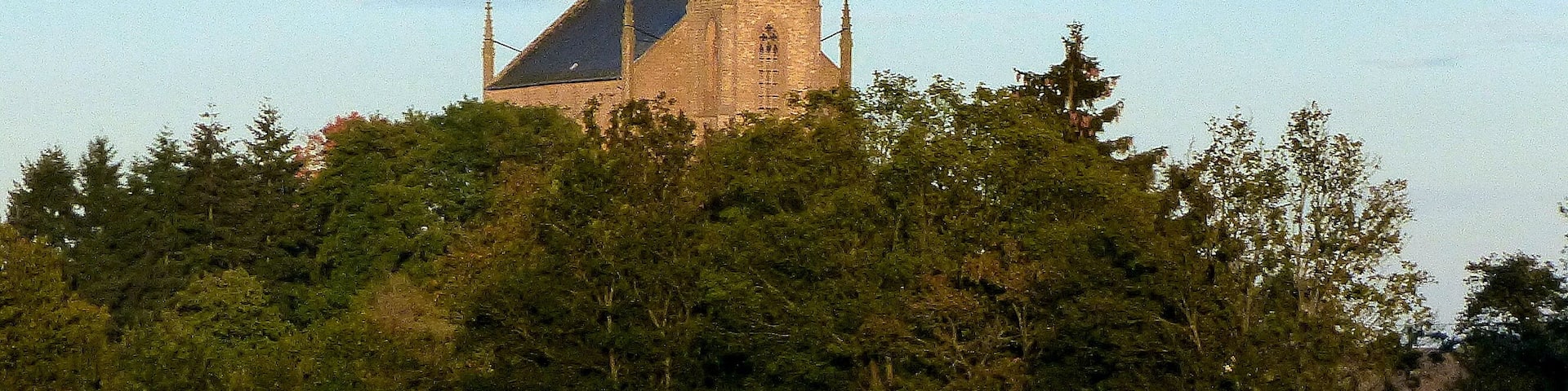 A church with a tall spire and clock tower, surrounded by trees.