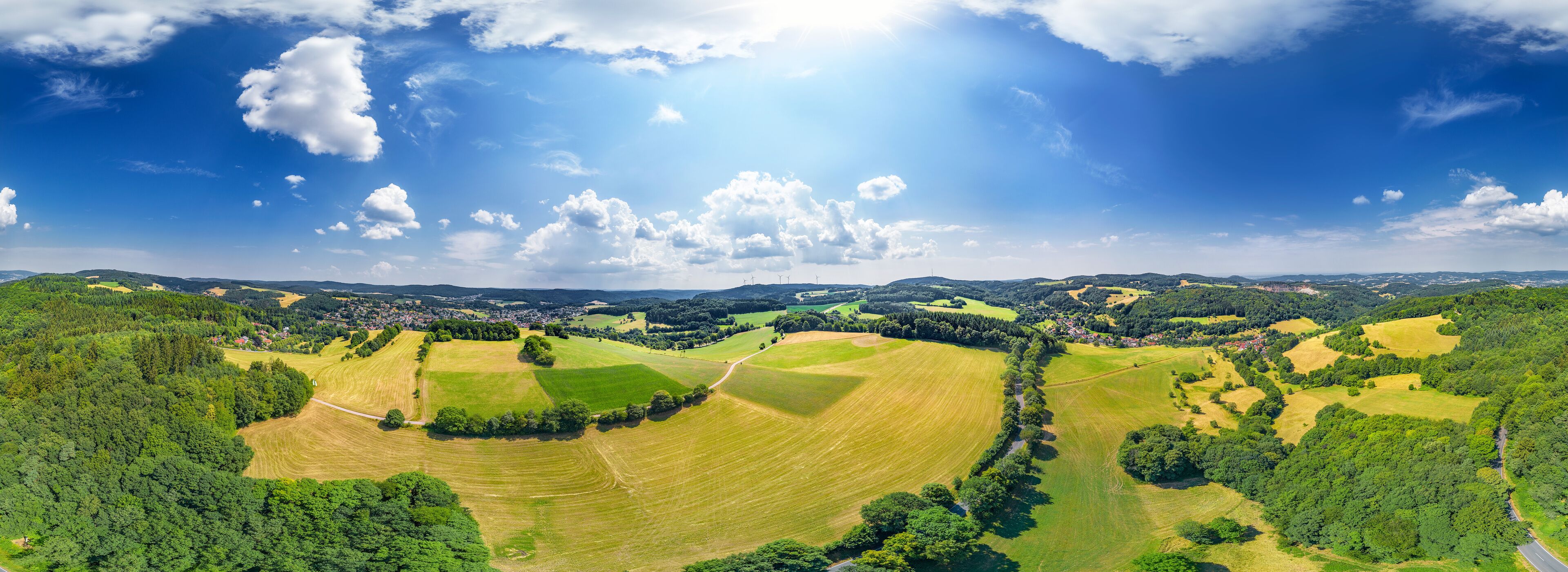 A panoramic view of a rural landscape with rolling hills, fields, and scattered trees.
