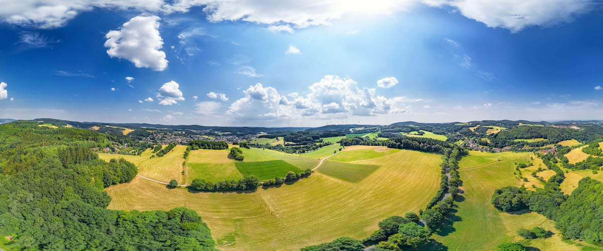 A panoramic view of a rural landscape with rolling hills, fields, and scattered trees.
