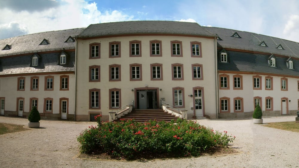Un grand bâtiment historique à la façade symétrique, doté de nombreuses fenêtres et d’une entrée centrale avec des marches.