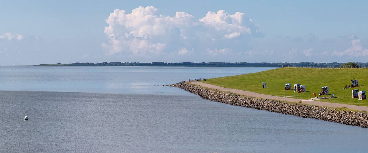 A calm lake with a grassy shore and a few people in the distance.