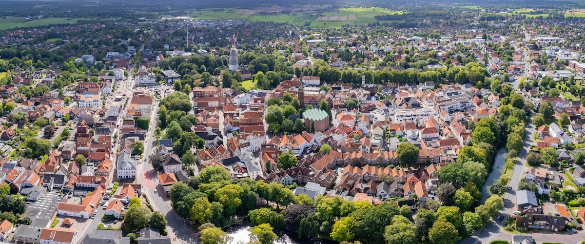An aerial view of a town with a river, surrounded by green fields and residential areas.