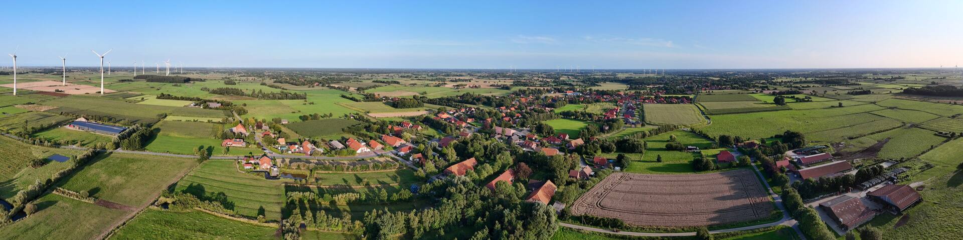 A rural landscape with wind turbines, fields, and a small village.
