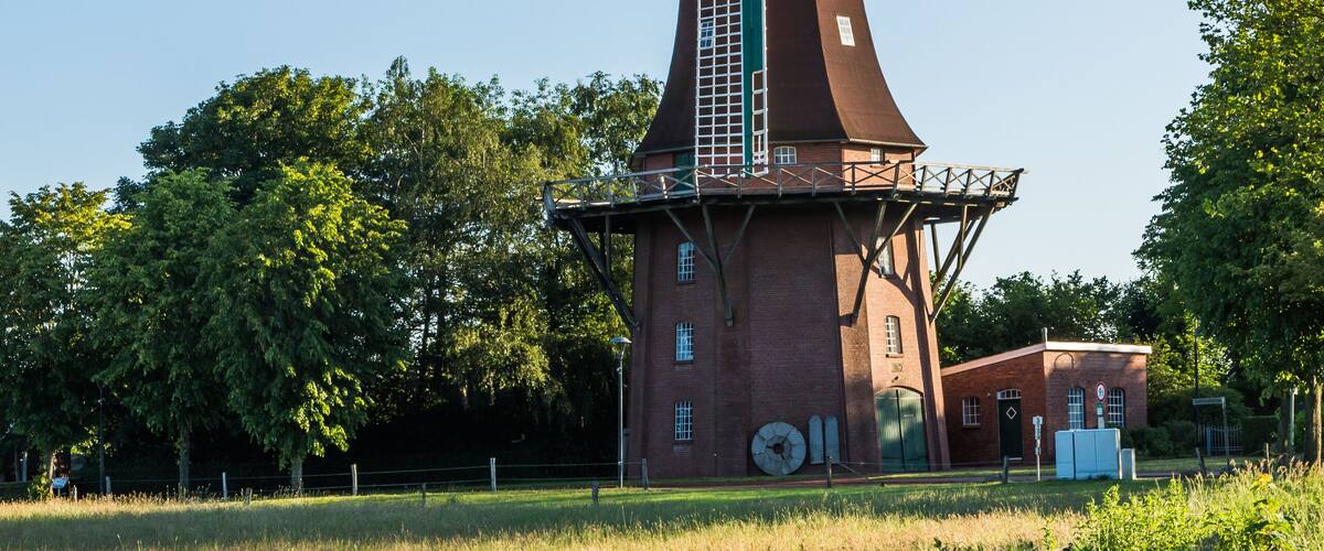 A traditional windmill with a lattice structure, surrounded by a grassy field and trees.