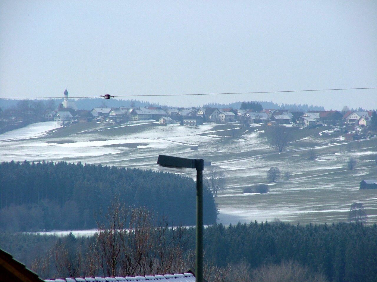 A snowy landscape with a streetlight, houses, and a distant church tower.