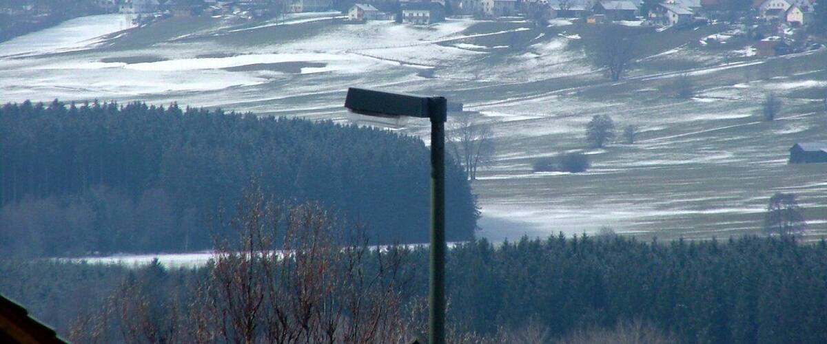 A snowy landscape with a streetlight, houses, and a distant church tower.