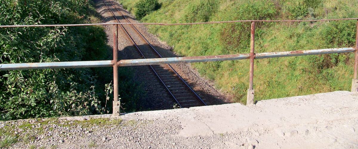 A railway track running through a rural landscape with greenery and open fields.