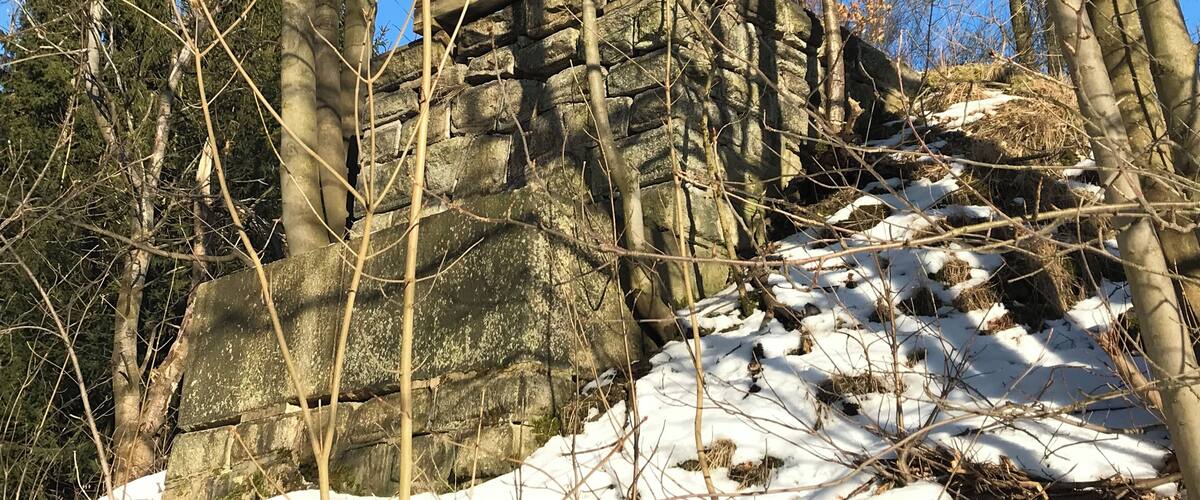 A rocky outcrop surrounded by leafless trees and patches of snow.