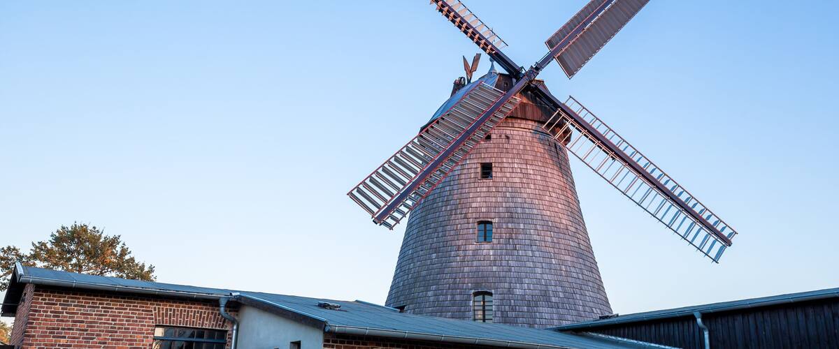 A windmill with a brick base and metal blades, set against a clear sky.