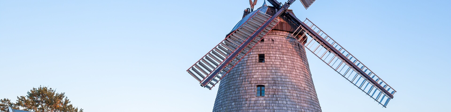 A windmill with a brick base and metal blades, set against a clear sky.