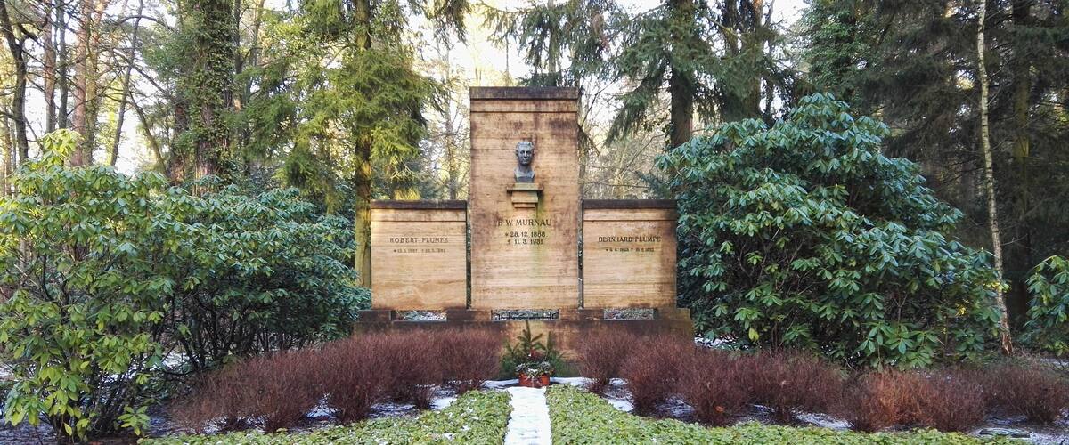 A memorial with inscriptions and a central bust, surrounded by a symmetrical garden with a gravel path.