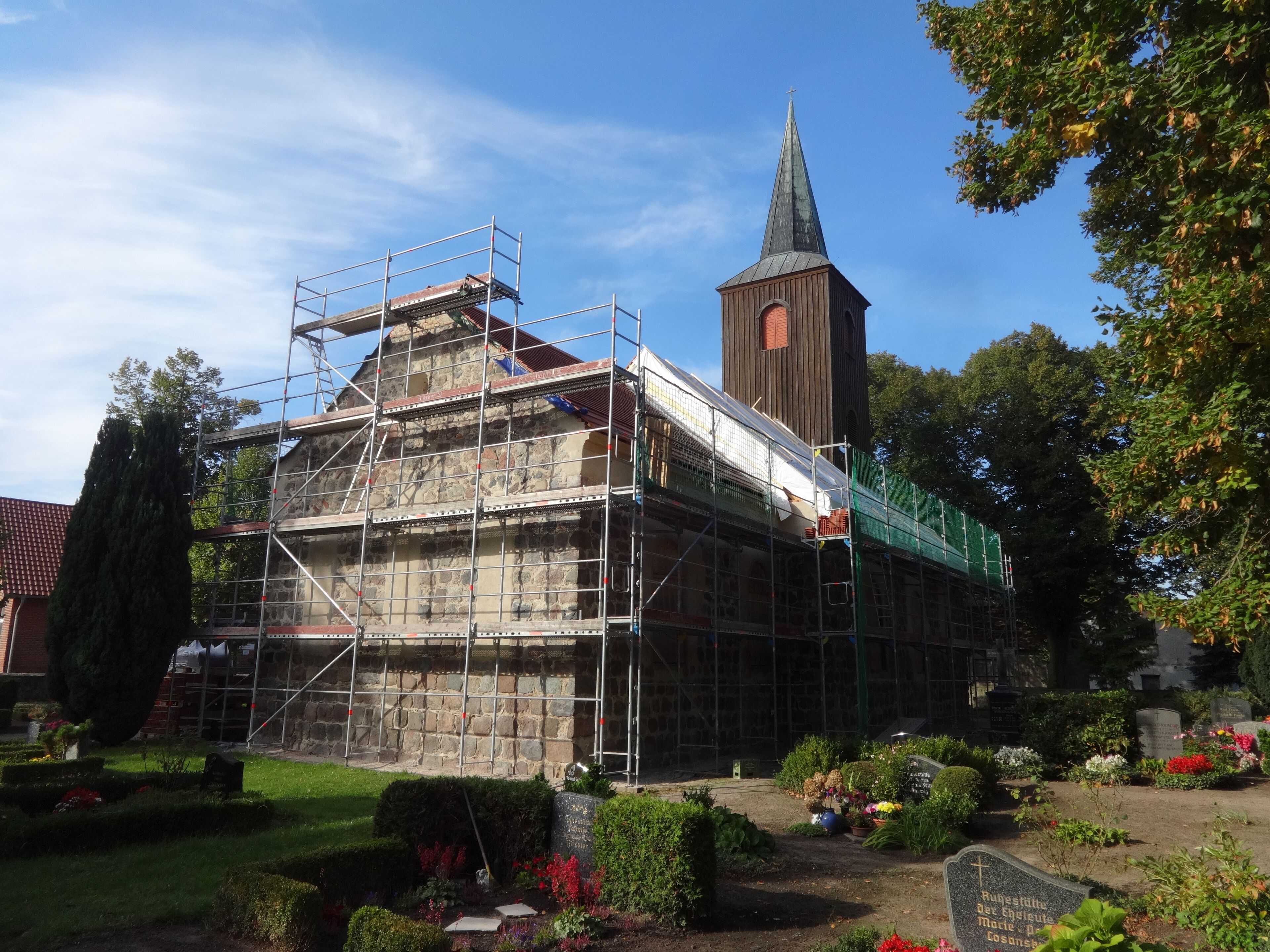 A church under construction with scaffolding, a steeple, and a cemetery with headstones.