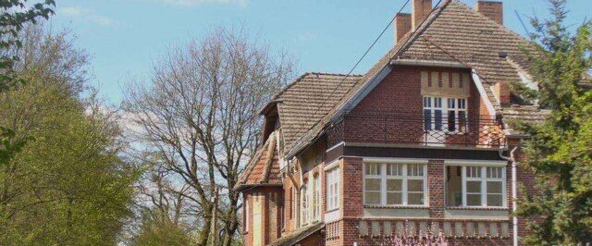 A brick house with a gabled roof, a gated driveway, and a fence.