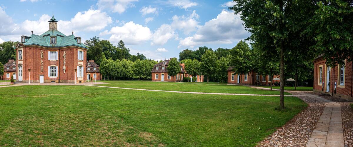 A large brick building with a green roof, surrounded by a well-maintained lawn and trees.