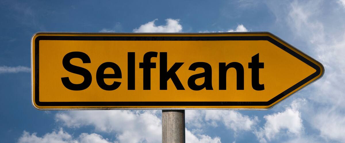 A directional sign with the word "Selfkant" against a blue sky with clouds.