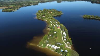 An aerial view of a narrow, elongated island with houses and greenery, surrounded by calm water.