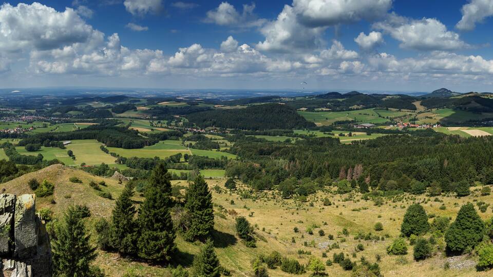 A panoramic view of a mountainous landscape with rolling hills, scattered trees, and a distant village.