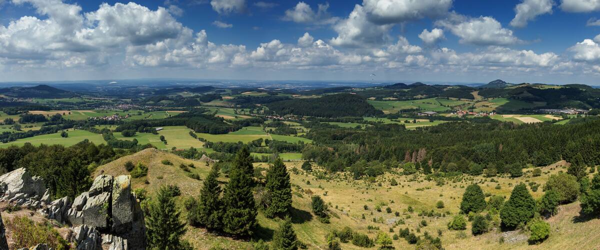 A panoramic view of a mountainous landscape with rolling hills, scattered trees, and a distant village.