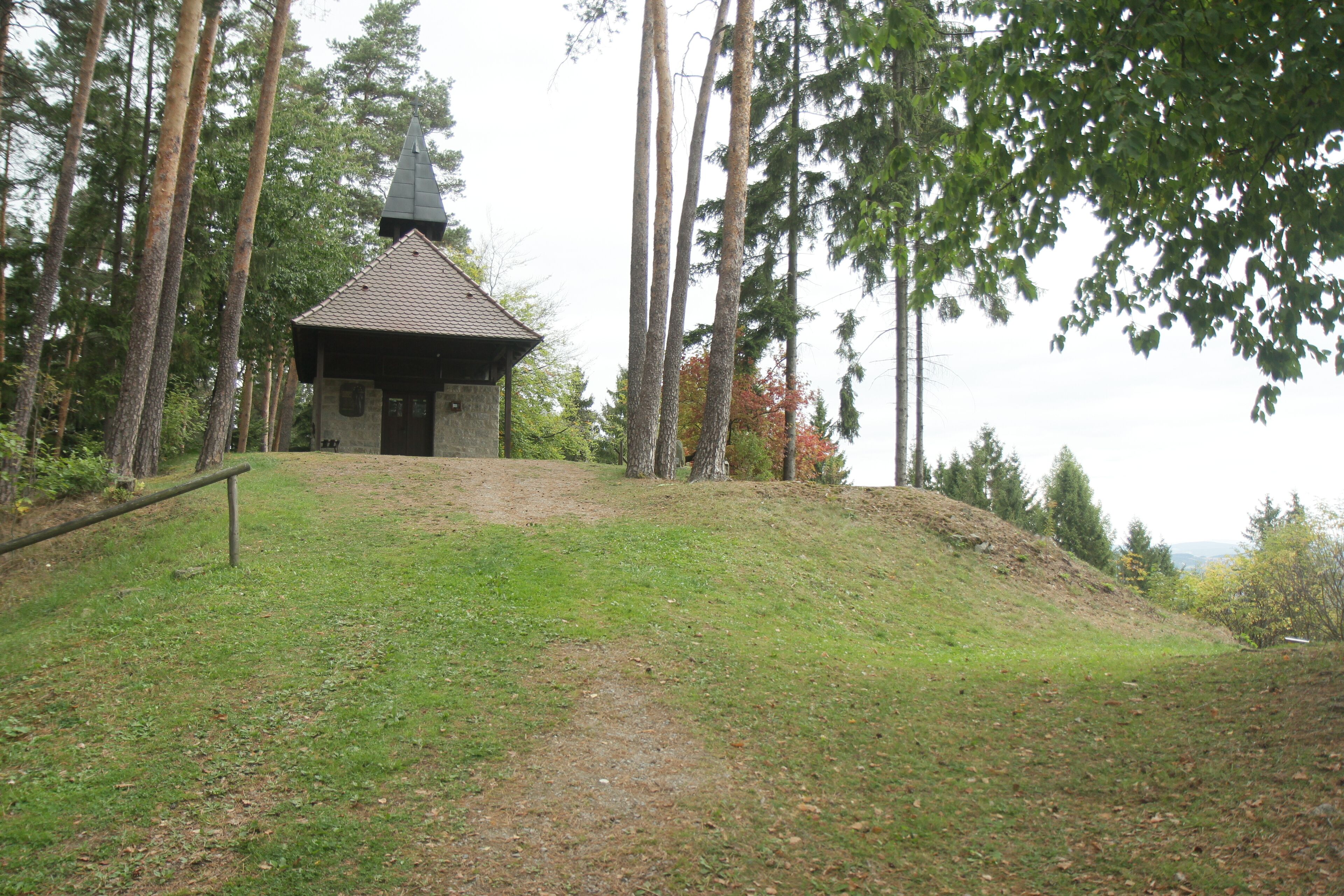A small stone chapel with a pointed roof surrounded by tall trees.