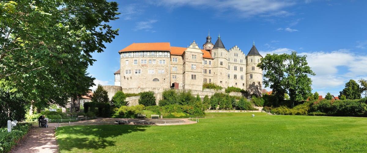 A large castle with a red roof, surrounded by green grass and trees.