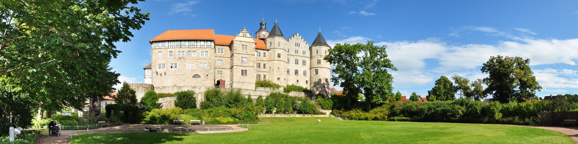 A large castle with a red roof, surrounded by green grass and trees.