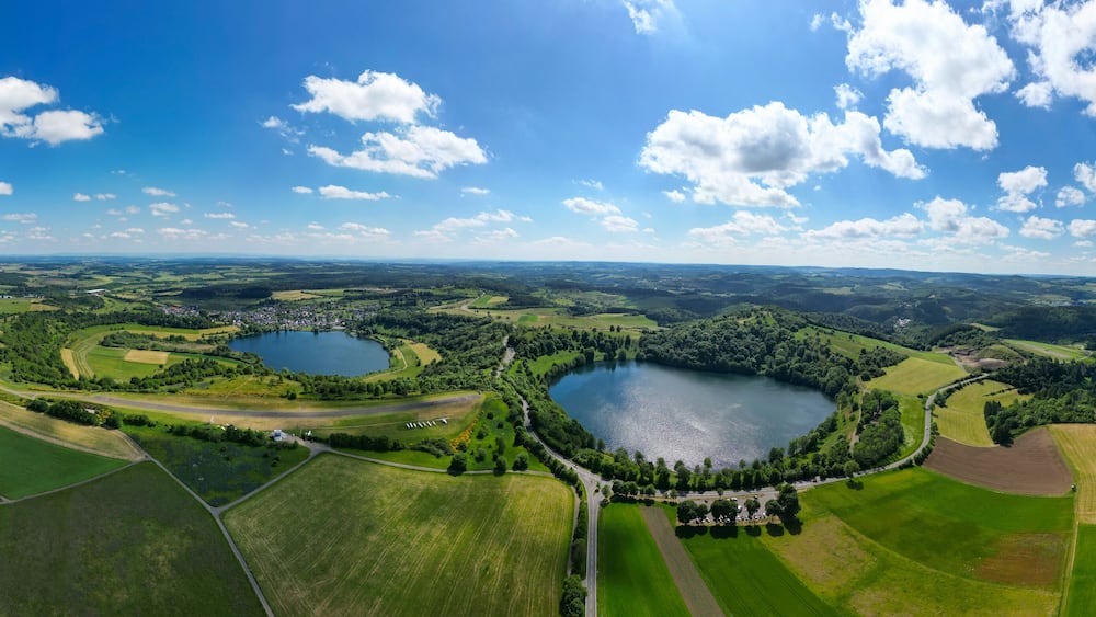 A panoramic view of a lake surrounded by green fields and a small town.