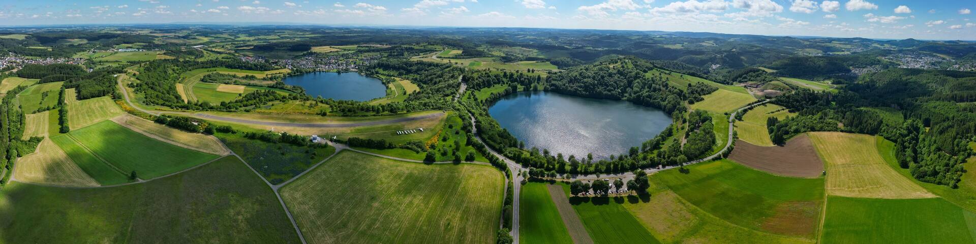 A panoramic view of a lake surrounded by green fields and a small town.
