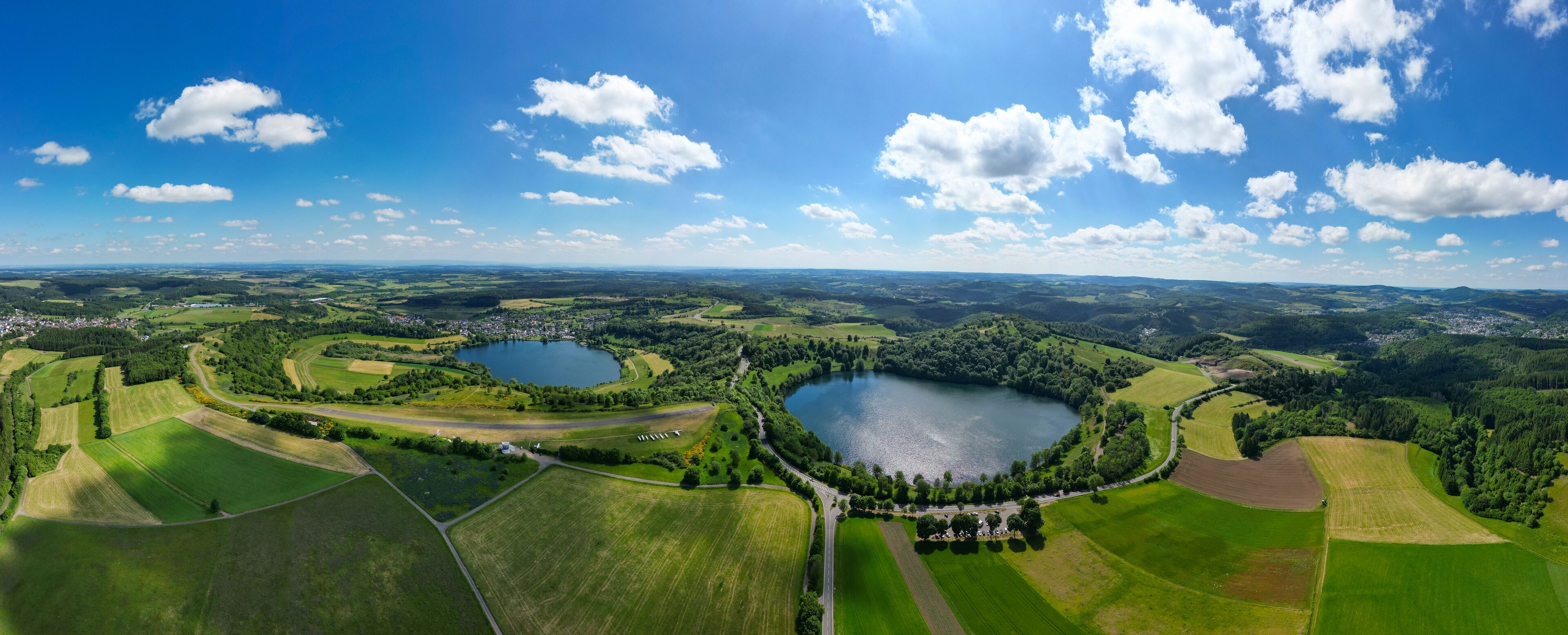 A panoramic view of a lake surrounded by green fields and a small town.