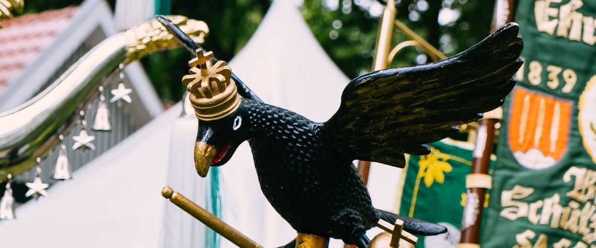 A black bird statue with wings and a crown, perched on a golden pole.