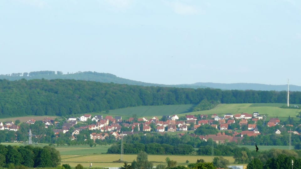 A rural village nestled in rolling hills with red-roofed houses and a prominent church spire.