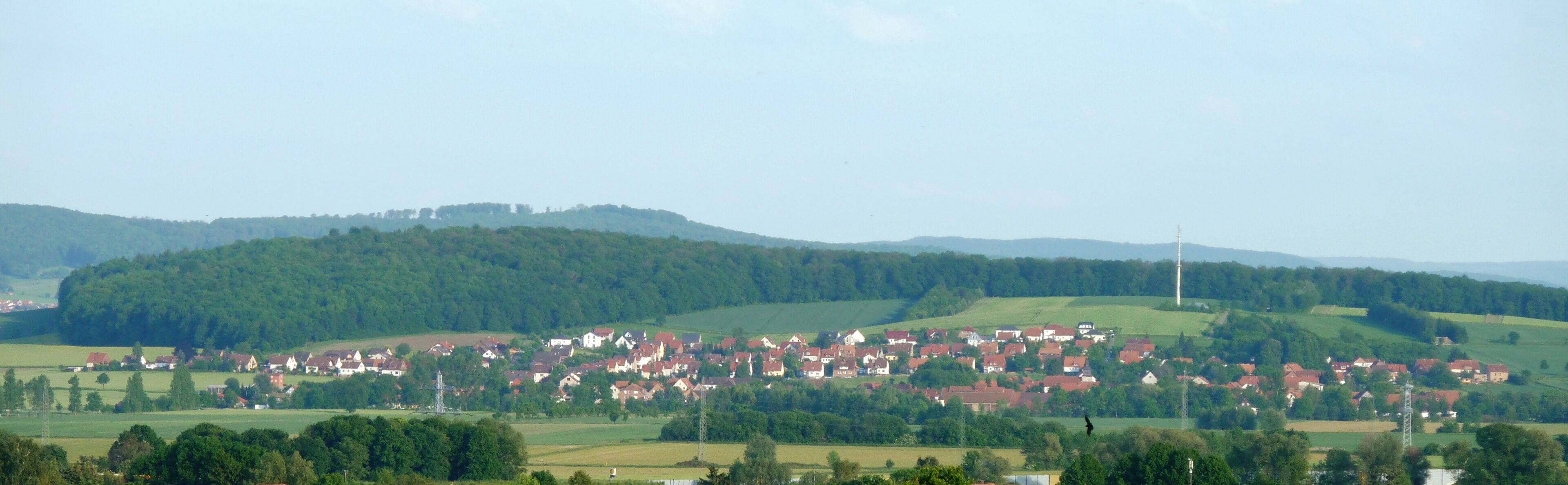 A rural village nestled in rolling hills with red-roofed houses and a prominent church spire.