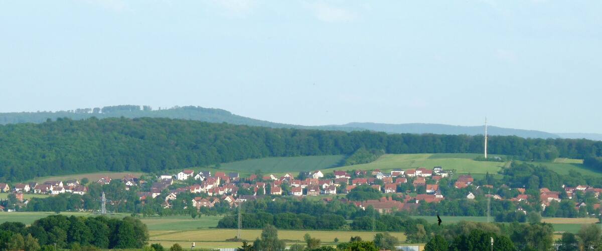 A rural village nestled in rolling hills with red-roofed houses and a prominent church spire.