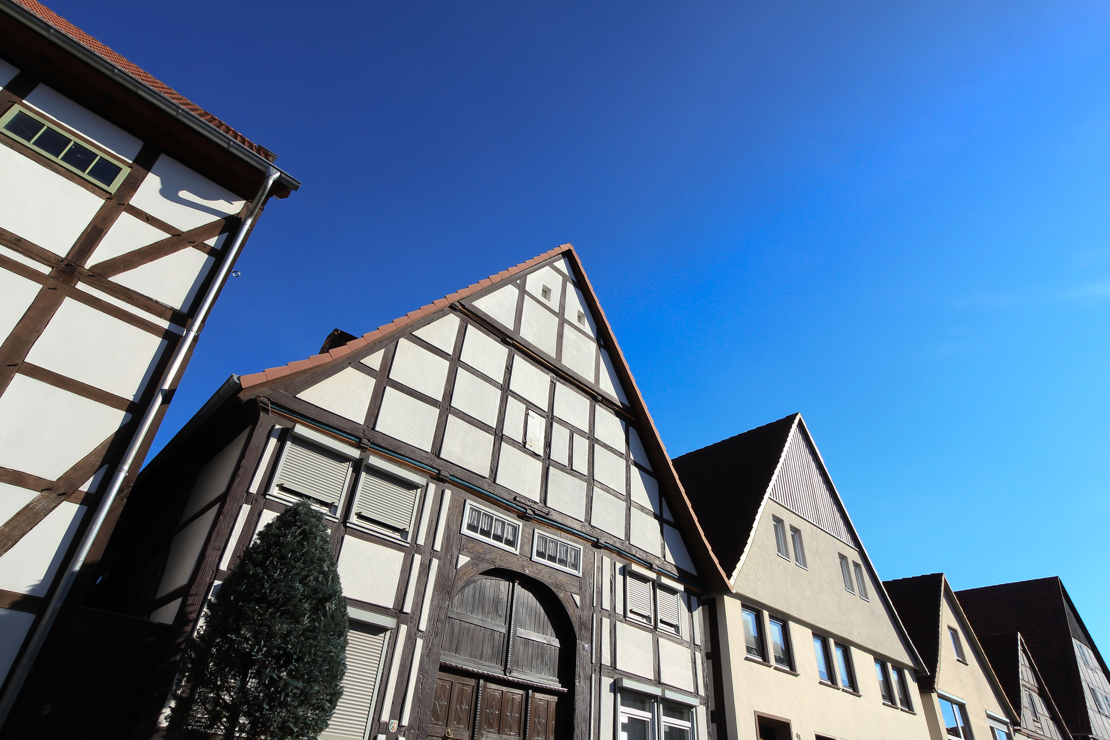 A traditional half-timbered building with a steeply pitched roof, a large arched entrance, and a small window with shutters.
